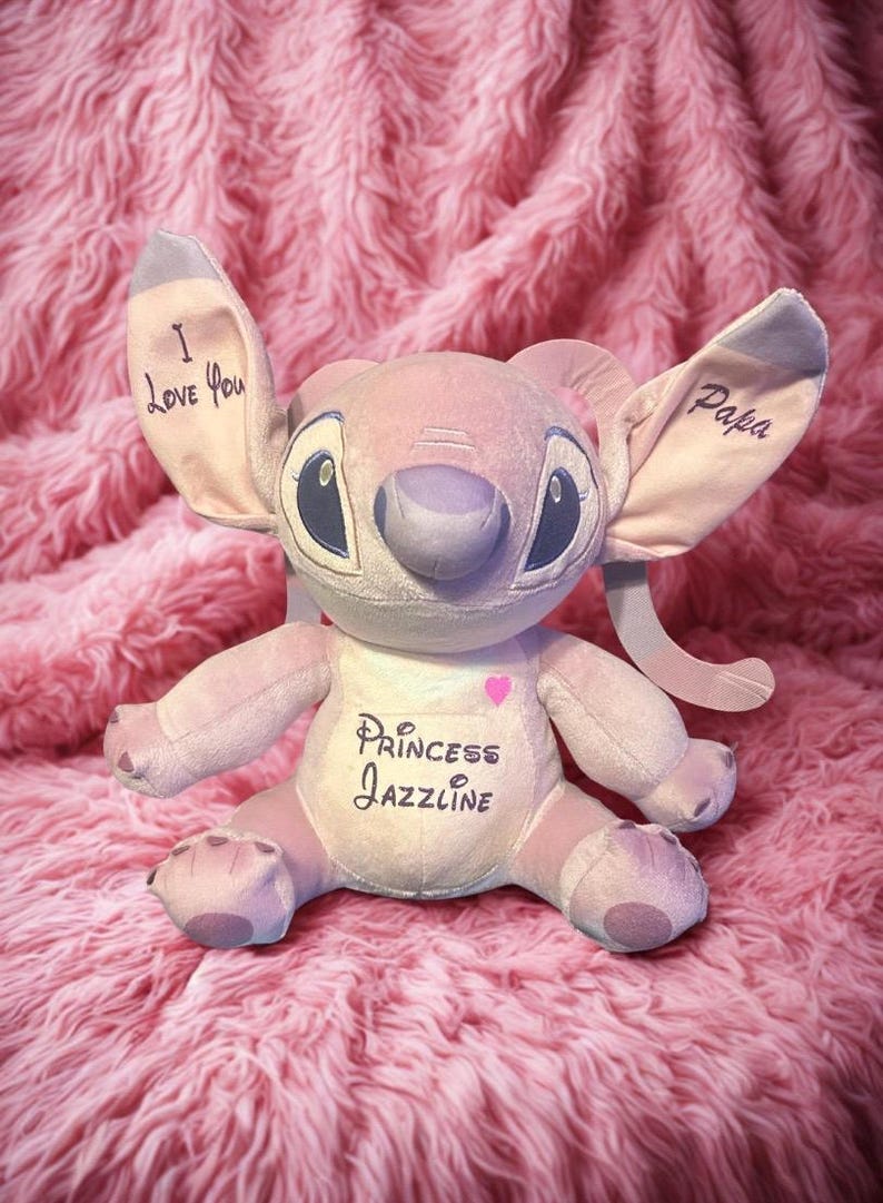 May include: A pink plush toy with large ears, blue eyes, and a grey nose. The ears have the words "I Love You" and "Papa" written on them. The toy's chest has the words "Princess Jazzline" and a pink heart.