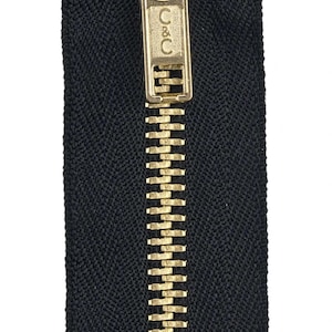 Puede incluir: Una cremallera negra con un deslizador y una lengüeta de metal dorado. El deslizador tiene el texto "C&C" grabado.