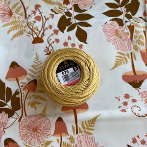 May include: A spool of DMC embroidery floss in a light gold color. The spool is labeled with the DMC number 676 and the color name "Golden Yellow".