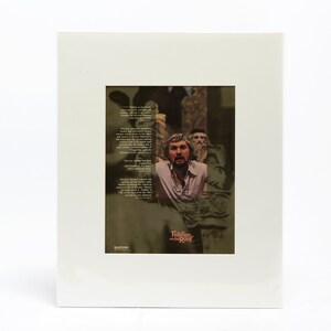 May include: A framed poster with a black and white photo of a man with a beard and a white shirt. The poster has a green background with text about the play "Tiddler and the Other."