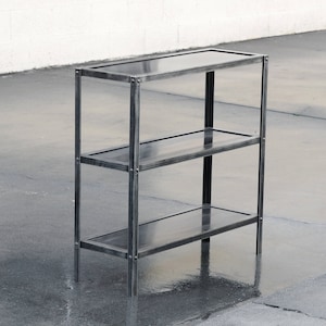 May include: A black metal shelving unit with three shelves. The shelves are made of metal and have a black finish.