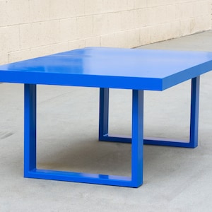 May include: A modern, square-shaped table in a vibrant blue hue. The table has a solid, flat top and four square legs. The table measures approximately 48 inches long, 48 inches wide, and 16 inches high.