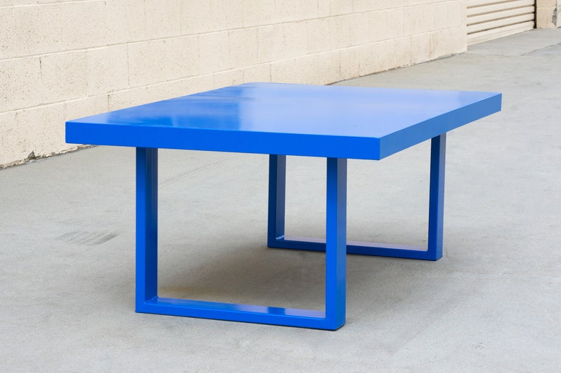 May include: A modern, square-shaped table in a vibrant blue hue. The table has a solid, flat top and four square legs. The table measures approximately 48 inches long, 48 inches wide, and 16 inches high.
