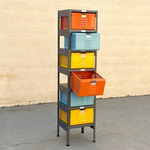 May include: A six-tier metal storage unit with colorful drawers. The drawers are orange, blue, yellow, and orange. The unit is made of metal and has a black frame. The drawers are open and show the interior of the unit.