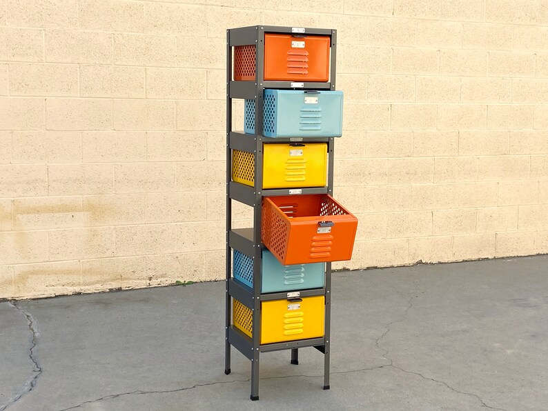 May include: A six-tier metal storage unit with colorful drawers. The drawers are orange, blue, yellow, and orange. The unit is made of metal and has a black frame. The drawers are open and show the interior of the unit.