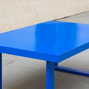 May include: A rectangular table with a vibrant blue finish. The table has a solid, flat top and sturdy, square legs. The table's dimensions are approximately 60 inches long, 30 inches wide, and 30 inches high.