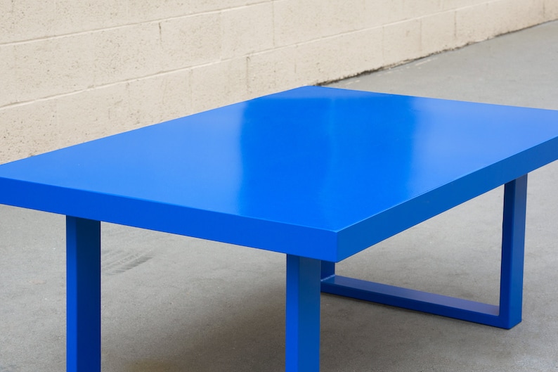 May include: A rectangular table with a vibrant blue finish. The table has a solid, flat top and sturdy, square legs. The table's dimensions are approximately 60 inches long, 30 inches wide, and 30 inches high.