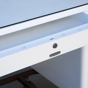 May include: White metal desk with a drawer that has a built-in organizer and a keyhole. The drawer is open and the desk has a glass top.