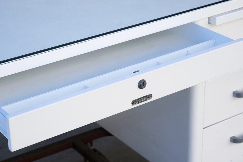 May include: White metal desk with a drawer that has a built-in organizer and a keyhole. The drawer is open and the desk has a glass top.
