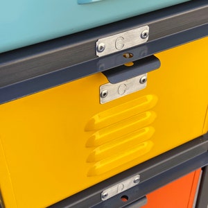 May include: A yellow metal locker with a black metal frame and a handle. The locker has a metal label with the letter "C" on it. The locker is part of a stack of lockers.