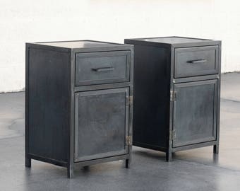 May include: Two black metal nightstands with a drawer and a door. Each nightstand has a simple design with a metal handle.