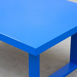 May include: A modern, bright blue table with a rectangular top and square legs. The table is painted in a solid, vibrant blue color. The table's dimensions are not visible in the image.