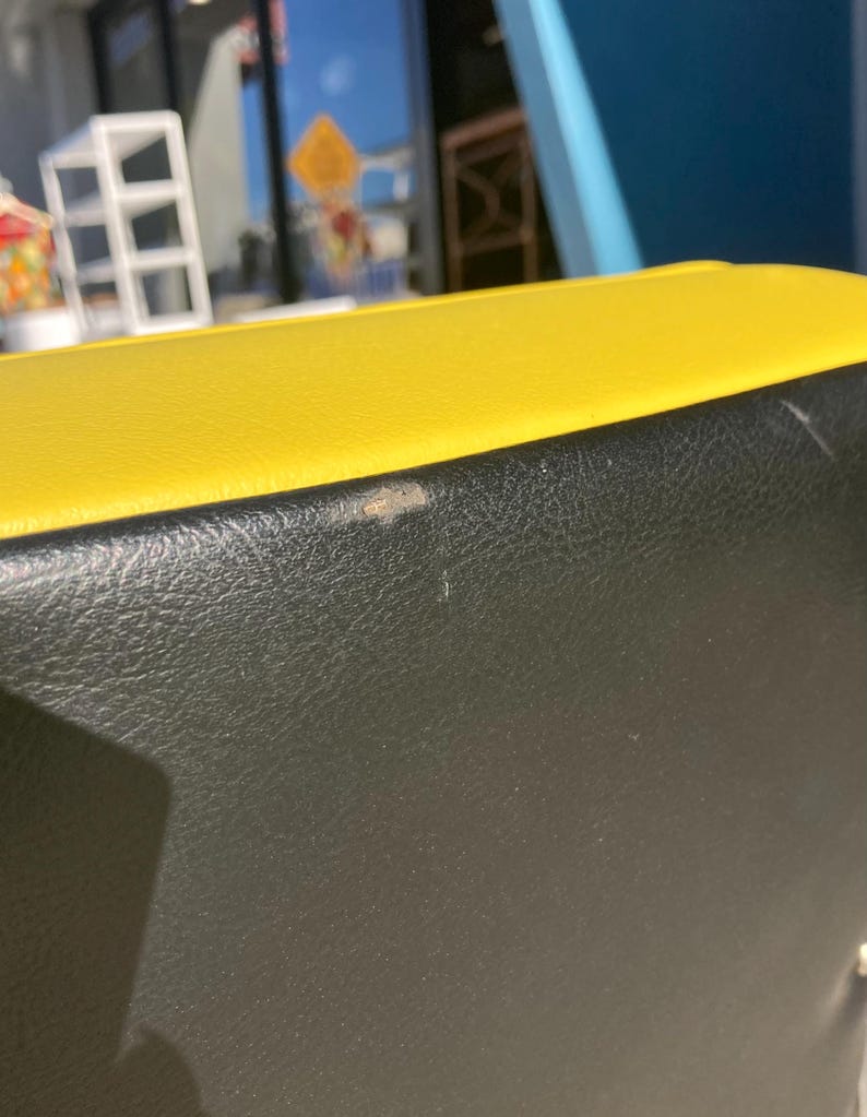 Op de afbeelding: Close-up van een geel en zwart leren object. De bovenkant is felgeel en de onderkant is zwart. Het leer heeft een getextureerde uitstraling. Er zijn een paar kleine onvolkomenheden op het zwarte oppervlak.