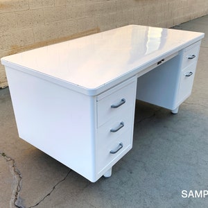 May include: White metal desk with three drawers on the left side and two drawers on the right side. The desk has a white laminate top.