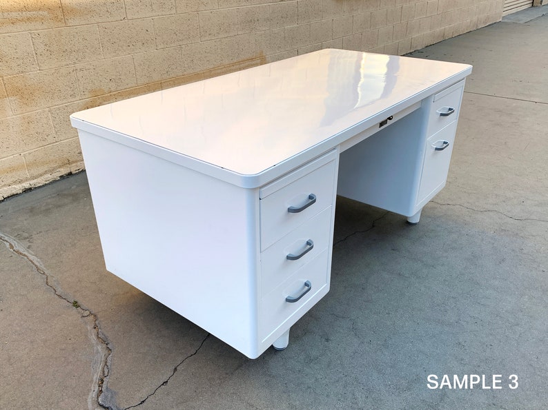May include: White metal desk with three drawers on the left side and two drawers on the right side. The desk has a white laminate top.