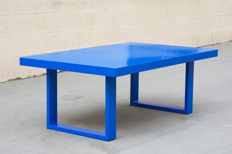 May include: A vibrant blue rectangular coffee table. The table has a solid, flat top and four square legs. The table is approximately 48 inches long, 24 inches wide, and 16 inches high.