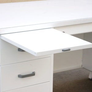 May include: White metal desk with a pull-out drawer and three drawers. The desk has a white metal top and a white metal pull-out drawer. The desk has three drawers with silver handles.
