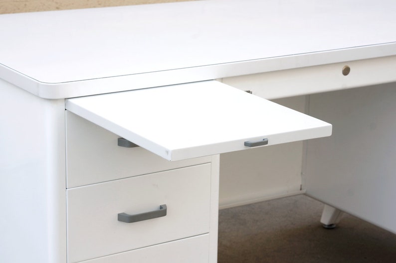 May include: White metal desk with a pull-out drawer and three drawers. The desk has a white metal top and a white metal pull-out drawer. The desk has three drawers with silver handles.