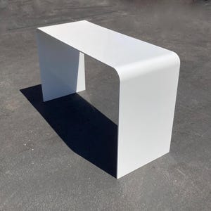 Op de afbeelding: Een witte, moderne consoletafel met een gebogen, rechthoekig blad en een eenvoudig, minimalistisch ontwerp.