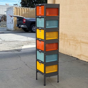 May include: A six-tier metal storage unit with colorful drawers and wire mesh fronts. The drawers are painted in shades of orange, yellow, blue, and green. The unit has a dark gray metal frame and stands on four black legs.