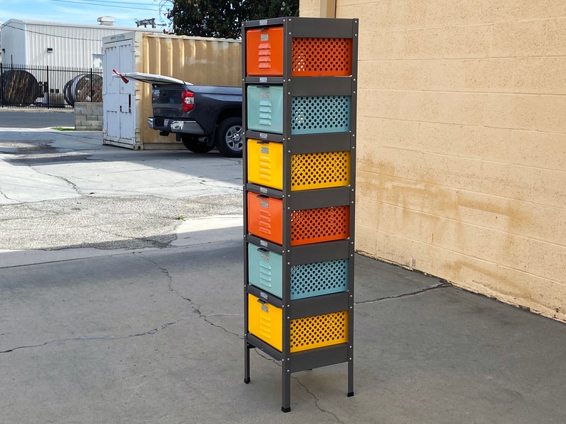 May include: A six-tier metal storage unit with colorful drawers and wire mesh fronts. The drawers are painted in shades of orange, yellow, blue, and green. The unit has a dark gray metal frame and stands on four black legs.