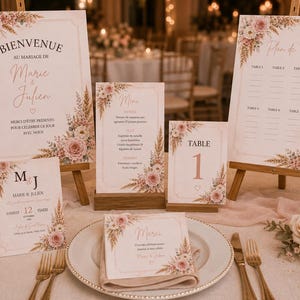 May include: A wedding stationery set featuring a welcome sign, table plan, menu, table number, and place cards. Each piece is decorated with floral illustrations of pink roses and pampas grass, with text including "Bienvenue," "Plan de Table," and "Marie & Julien."