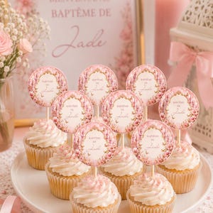 May include: A display of cupcakes with pink frosting and decorative toppers. The toppers feature a floral design and the text "Baptême de Jade." A sign in the background reads "Bienvenue au Baptême de Jade."