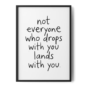 May include: A rectangular wall art print in a thin black frame featuring a white background with the black text: not everyone who drops with you lands with you. The lettering is in a simple, handwritten style with small ink-like speckles.