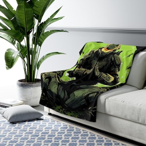 May include: A plush throw blanket featuring a vibrant graphic illustration of a futuristic soldier in dark green armor. The character is depicted in a seated, meditative pose against a bright lime green background with abstract black ink-style accents.