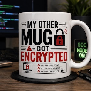 May include: White ceramic mug with the text "MY OTHER MUG GOT ENCRYPTED" in black and red. The mug features a lock graphic and a list of IT-related issues. A black coaster sits beneath the mug. The background includes a computer monitor and a "SOC MODE ON" sign.