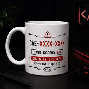May include: White ceramic mug with a black handle, featuring a tech-themed design. The mug displays the text "CVE-XXXX-XXXX", "CVSS SCORE: 9.8", and "SEVERITY: CRITICAL". The design includes a warning symbol and the phrase "<CAFFEINE REQUIRED>".