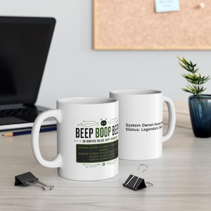 Può includere: Due tazze in ceramica bianca con testo e grafica in nero e verde. Una tazza riporta il testo BEEP BOOP BEEP OR HOWEVER YOU SAY HAPPY FATHERS DAY con codice binario. L'altra mostra System Owner: Name Here Status: Legendary Dad.