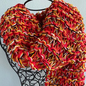May include: A red, yellow, white and black knitted scarf with a chunky knit texture.