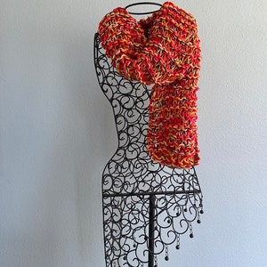 May include: A red, yellow and white knitted scarf displayed on a black metal mannequin.