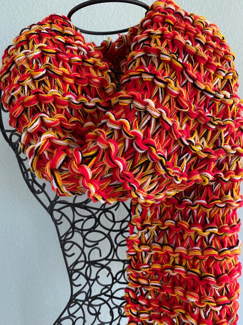 May include: A red, yellow, white and black knitted scarf with a chunky knit texture.