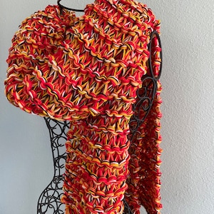 May include: A chunky knit scarf in red, yellow, black and white. The scarf is draped over a black metal mannequin.