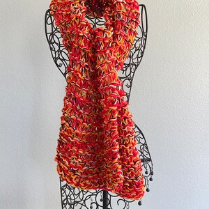 May include: A red, yellow and white knitted scarf with a fringe of black beads.