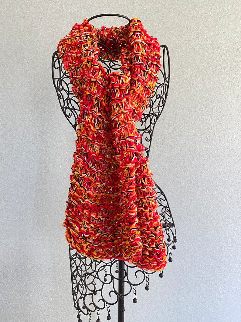 May include: A red, yellow and white knitted scarf with a fringe of black beads.