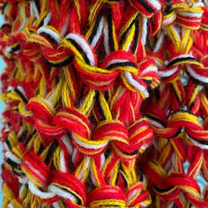 May include: Close-up of a woven fabric with red, yellow, white and black yarn. The fabric is made with a simple weave pattern and has a textured surface.