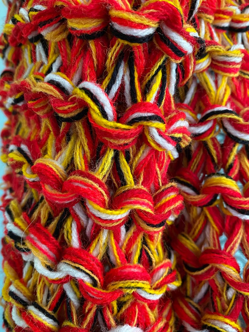 May include: Close-up of a woven fabric with red, yellow, white and black yarn. The fabric is made with a simple weave pattern and has a textured surface.