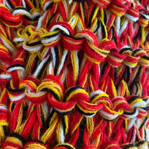 May include: Close-up of a woven fabric with red, yellow, white and black threads. The threads are woven together in a complex pattern, creating a textured surface.