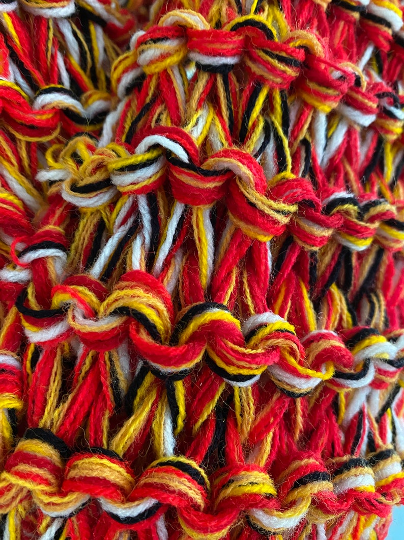 May include: Close-up of a woven fabric with red, yellow, white and black threads. The threads are woven together in a complex pattern, creating a textured surface.