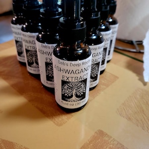 Pu&ograve; includere: Una collezione di bottiglie di vetro marrone con contagocce neri. Ogni bottiglia ha un'etichetta bianca con il testo "Deb's Deep Roots ASHWAGAND EXTRACT" e una grafica ad albero. Le bottiglie contengono 30 ml.
