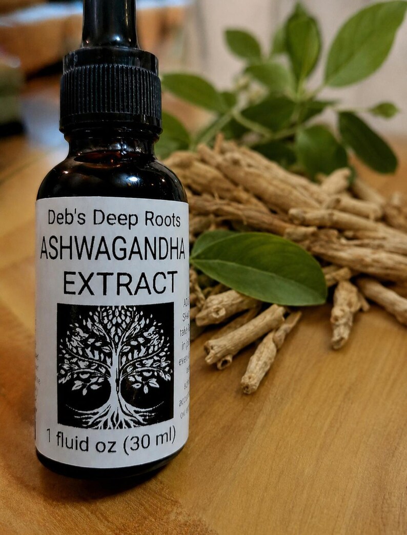 Pu&ograve; includere: Una bottiglia di vetro nero di estratto di Ashwagandha Deb's Deep Roots con un contagocce. L'etichetta presenta un disegno ad albero. La bottiglia &egrave; da 30 ml. Radici di Ashwagandha e foglie verdi sullo sfondo.