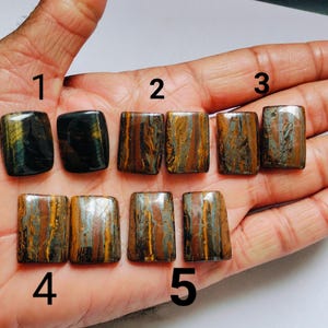 May include: Ten rectangular tiger's eye gemstones arranged in two rows, labeled with numbers 1 through 5. The stones display varied patterns of golden-brown, black, and blue-grey chatoyant bands with a polished, smooth, and reflective surface finish.