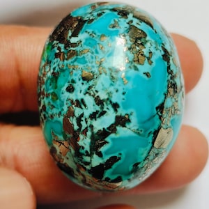 May include: An oval-shaped polished gemstone featuring a vibrant turquoise blue base colour with intricate, scattered metallic gold-toned pyrite inclusions and dark black matrix veins throughout the smooth, reflective surface of the stone.