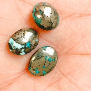 Puede incluir: Tres cabujones de forma ovalada con una superficie pulida que presenta una mezcla de matriz azul turquesa brillante e inclusiones de pirita en tonos dorados metálicos. Cada piedra muestra un patrón único de vetas naturales y minerales.