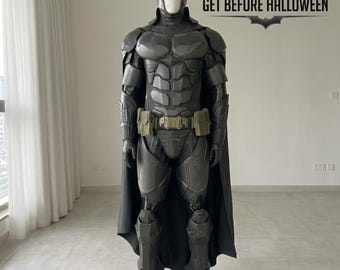 Könnte beinhalten: Ein dunkelgraues Batman-Kostüm in Ganzkörperausführung auf einer Schaufensterpuppe, bestehend aus geformtem Brustpanzer, Armschienen, Beinschutz, einem Gürtel mit olivgrünen Taschen und einem schwarzen Umhang. Der Text ORDER NOW GET BEFORE HALLOWEEN ist sichtbar.