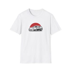 May include: A white short-sleeve t-shirt featuring a centered graphic illustration of a black and white sports car positioned in front of a solid red circle. The design is printed on the chest area of the plain white crew neck garment.