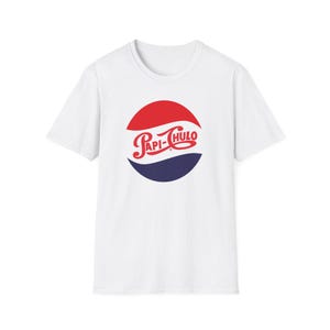 May include: A white short-sleeve t-shirt featuring a circular graphic on the chest. The graphic consists of a red upper semicircle and a dark blue lower semicircle, separated by a white wavy line. The text Papi-Chulo is written in red script.